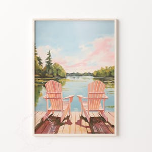 May include: A framed art print depicts two peach-colored Adirondack chairs on a wooden dock overlooking a calm lake. The sky is a soft blue with pink clouds, and trees line the distant shore. The artwork evokes a sense of peace and relaxation.