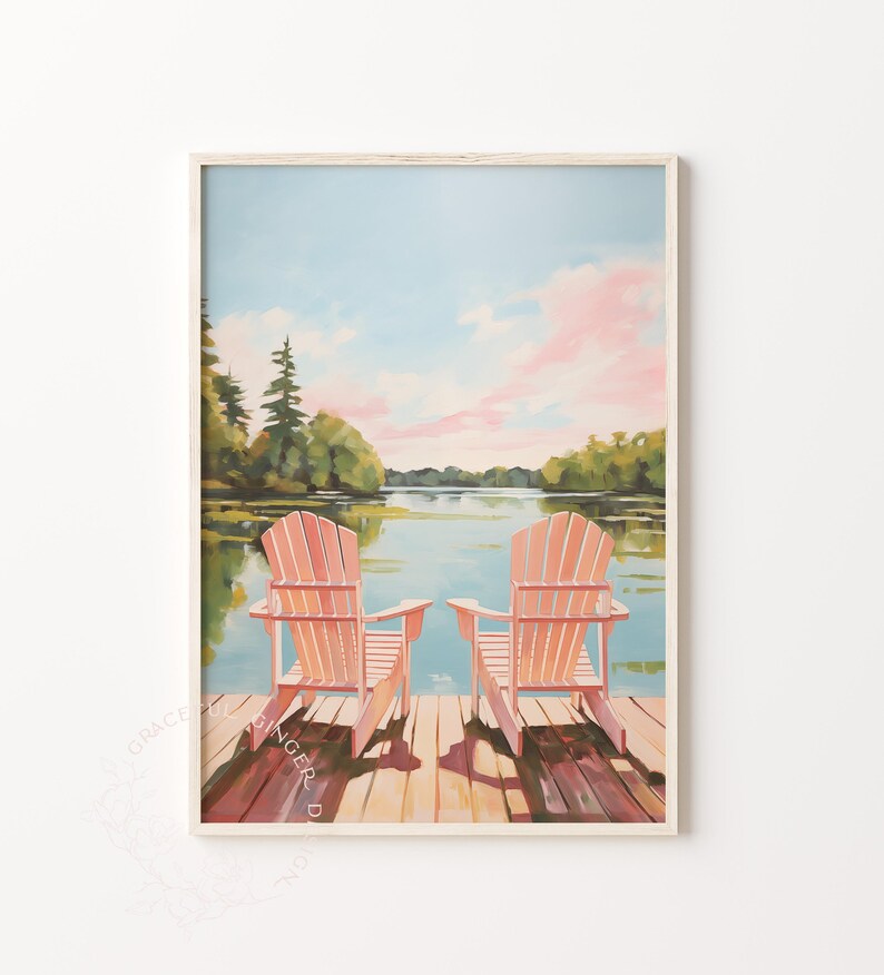 May include: A framed art print depicts two peach-colored Adirondack chairs on a wooden dock overlooking a calm lake. The sky is a soft blue with pink clouds, and trees line the distant shore. The artwork evokes a sense of peace and relaxation.