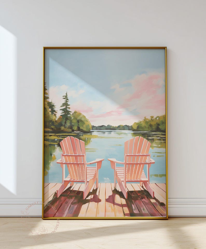 May include: A framed art print depicts two pink Adirondack chairs on a wooden dock overlooking a serene lake scene. The sky is a soft blue with pink clouds, and the artwork is framed in gold.
