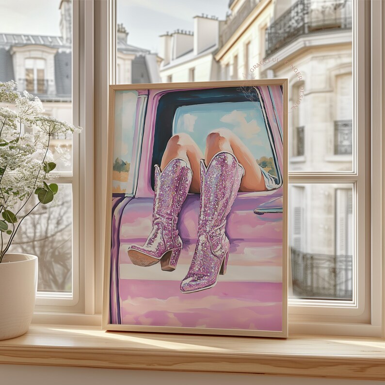 May include: A framed artwork depicts a person's legs and sparkly pink cowboy boots resting on a pink car. The boots have a high heel and are covered in glitter. The background shows a sunny sky and buildings.