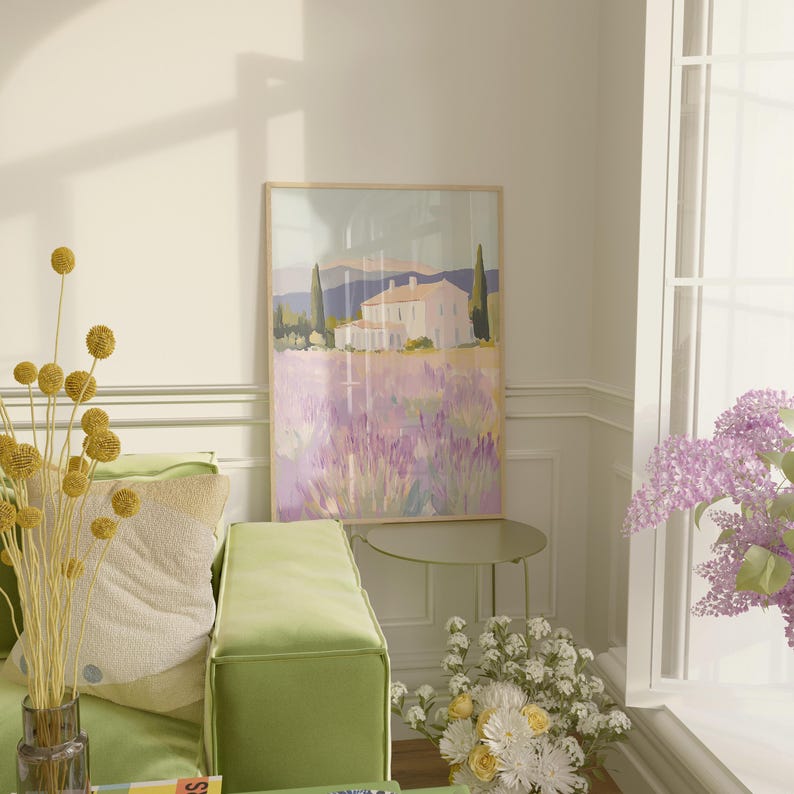 Artwork of a French-inspired villa and lavender fields leaning near a green sofa. Surrounded by fresh florals and soft morning light, the setting adds a vibrant touch to the cozy corner.