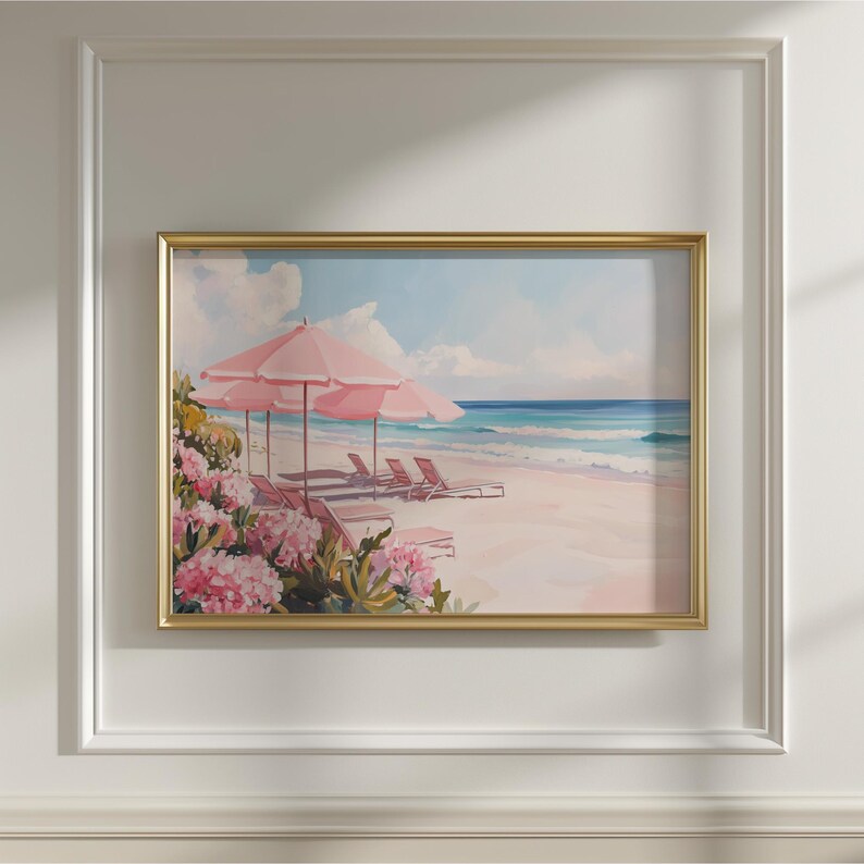 Beach painting with soft pink tones displayed inside a white paneled wall frame. The artwork shows a tropical shoreline with three blush umbrellas, ocean waves, and blooming pink flowers in the foreground.