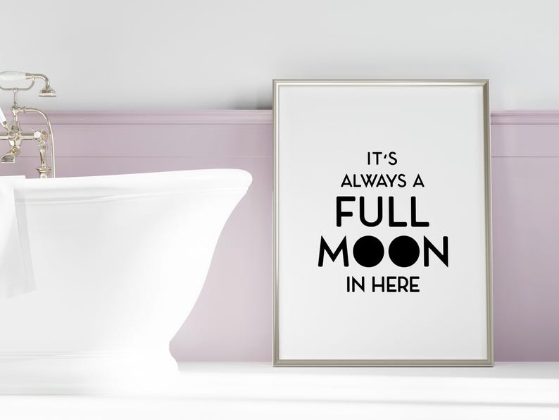 May include: A framed print with the text "IT'S ALWAYS A FULL MOON IN HERE" in black. The print is in a bathroom setting, next to a white bathtub and silver faucet.