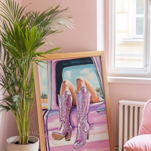 May include: A framed artwork depicts a person's legs and sparkly pink cowboy boots resting on a car door. The artwork is in a room with a pink wall, a potted plant, and a pink chair.