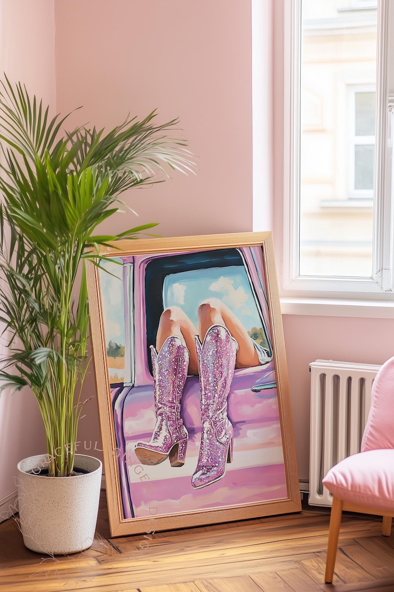May include: A framed artwork depicts a person's legs and sparkly pink cowboy boots resting on a car door. The artwork is in a room with a pink wall, a potted plant, and a pink chair.
