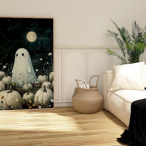 May include: A framed art print featuring a friendly ghost standing among pumpkins under a full moon. The artwork has a whimsical, cartoonish style with a dark, starry background. The pumpkins are white and the ghost is also white.