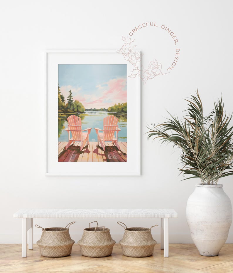 May include: A framed watercolor print depicts two pink Adirondack chairs on a wooden dock overlooking a lake. The sky is a blend of blue and pink, with trees lining the distant shore. The print is displayed above a white bench with three woven baskets.