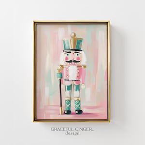 Puede incluir: Una lámina de arte enmarcada con un cascanueces pintado en tonos rosa, verde azulado y dorado. El cascanueces lleva un sombrero alto, una chaqueta con piel blanca y sostiene un bastón negro. El texto Graceful Ginger design aparece debajo.