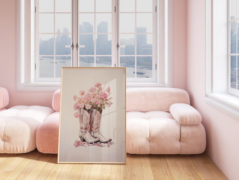 May include: A framed print of a still life featuring two white cowboy boots with pink flowers inside. The boots are on a white background with pink flower petals scattered around them.