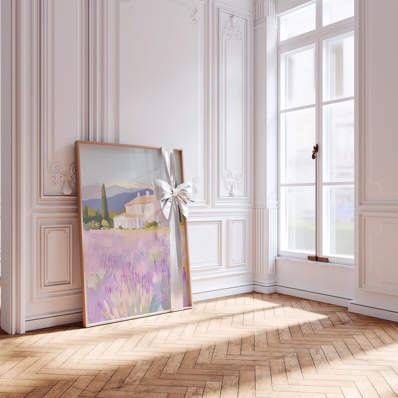 Framed lavender field painting with a silver ribbon bow, leaning near a bright window. The peaceful villa scene is bathed in sunlight, enhancing the soft purples and warm brushstrokes of the countryside landscape.