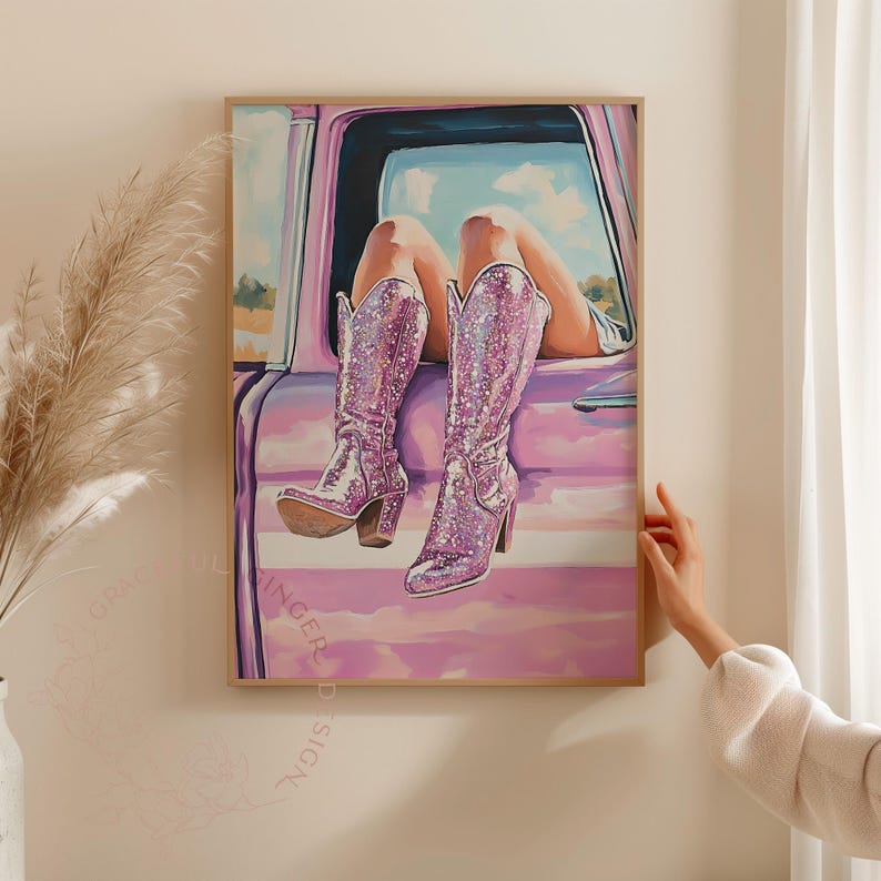 May include: A framed artwork depicts a pair of sparkling, high-heeled, pink cowboy boots. The boots are set against a pink car door, with legs visible through the open window. The artwork has a dreamy, whimsical feel.