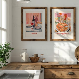 May include: Two framed prints hanging on a white tiled wall in a kitchen. The print on the left shows a glass of red wine and a bottle of wine on a table with the word "salute" written below. The print on the right shows a pizza with the words "buon appetito" written below.