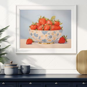 Op de afbeelding: Een witte kom met een blauw en geel bloemenpatroon gevuld met rode aardbeien. De kom staat op een lichtblauwe ondergrond met een enkele aardbei ervoor.