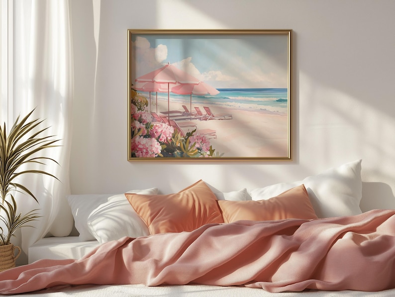 Beach-themed painting hung above a cozy bed styled with soft coral pillows and blankets. The art captures a pastel paradise with pink umbrellas and flowers beside an ocean shoreline, bathed in warm morning light.