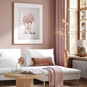 May include: A pink and white living room with a white couch, a pink throw blanket, a wooden coffee table, and a framed print of pink flowers in cowboy boots.