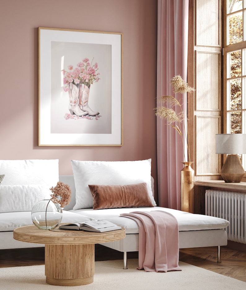 May include: A pink and white living room with a white couch, a pink throw blanket, a wooden coffee table, and a framed print of pink flowers in cowboy boots.