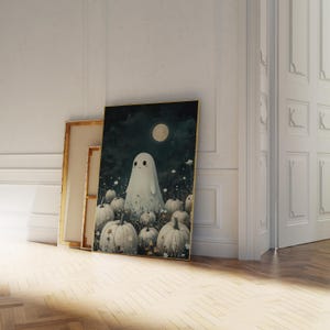 May include: A framed art print featuring a friendly ghost standing among pumpkins under a full moon. The artwork has a dark, whimsical aesthetic with a gold frame. The ghost is white, and the pumpkins are a light cream color.
