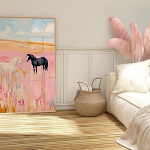 May include: A framed painting of two horses in a pink field. The horse on the left is white and the horse on the right is black. The painting is hanging on a white wall in a bedroom with a bed and a wicker basket.