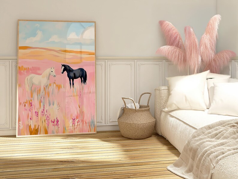 May include: A framed painting of two horses in a pink field. The horse on the left is white and the horse on the right is black. The painting is hanging on a white wall in a bedroom with a bed and a wicker basket.