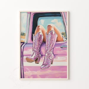 May include: A framed print of a woman's legs and sparkly pink cowboy boots hanging out of a pink car window. The boots have a high heel and are covered in glitter. The background shows a blue sky and a field.