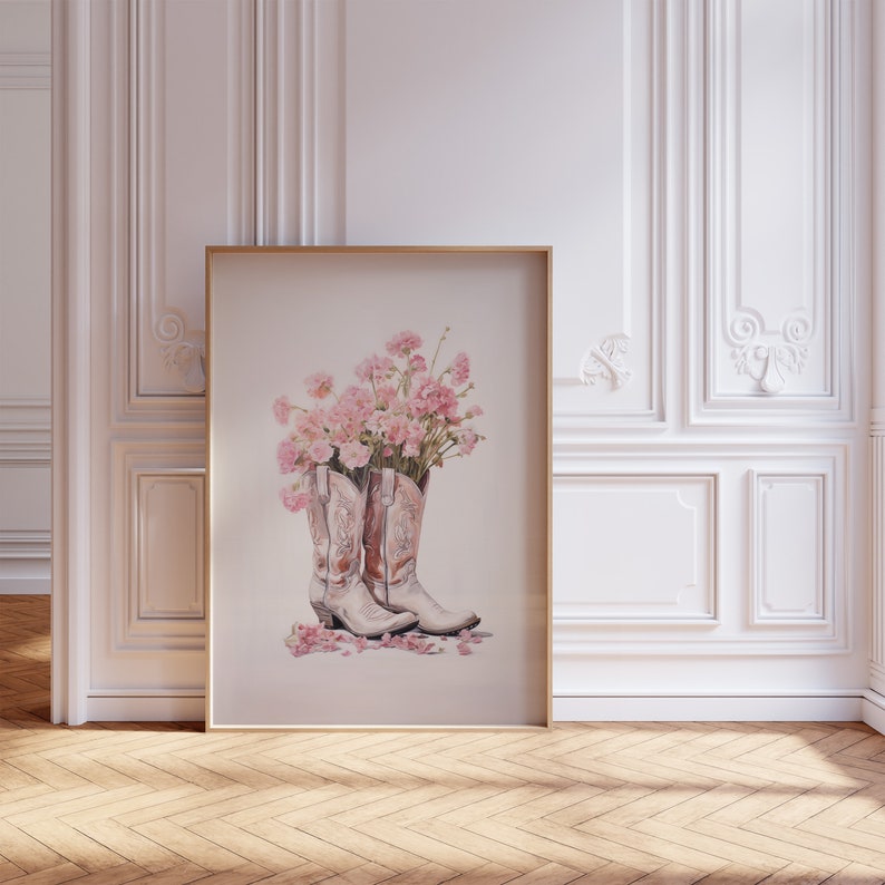 May include: A framed print of a watercolor painting of a pair of white cowboy boots with pink carnations inside. The boots are on a white background with pink petals scattered around them.