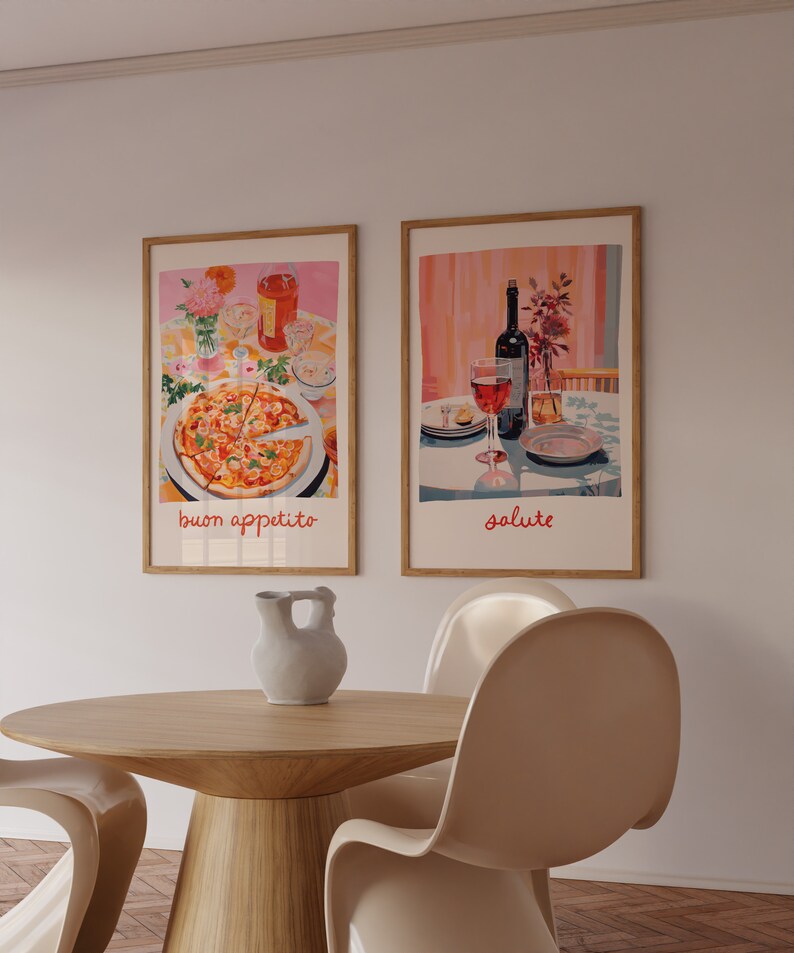 May include: Two framed prints on a white wall, one depicting a pizza with the text "buon appetito" and the other depicting a bottle of wine and two glasses with the text "salute". A wooden table with a ceramic pitcher and two white chairs are in the foreground.