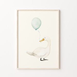 May include: Watercolor illustration of a white duck with a yellow beak, holding a light blue balloon. The artwork is framed in a light wood frame, perfect for a nursery or children's room. The background is a soft, off-white color.