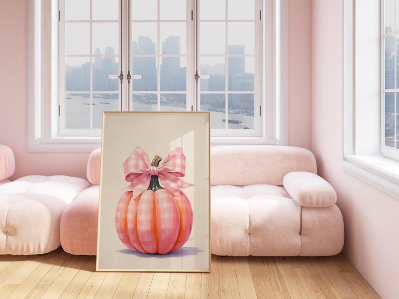 Puede incluir: Una impresi&oacute;n art&iacute;stica enmarcada que presenta una pintura a la acuarela de una calabaza rosa con un lazo de cuadros. La calabaza tiene un patr&oacute;n a cuadros y est&aacute; colocada sobre un fondo neutro. La obra de arte se exhibe en una habitaci&oacute;n luminosa con un sof&aacute; rosa.