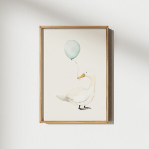May include: Watercolor illustration of a white goose holding a light blue balloon. The artwork is framed in a light brown wooden frame. The goose has a yellow beak and black feet. The balloon is tied to the goose's beak with a thin string. The background is a soft, off-white color.