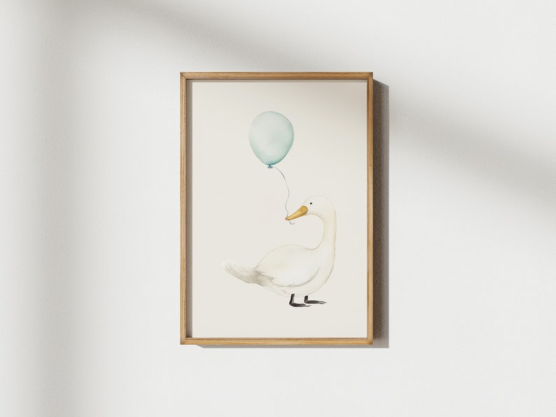 May include: Watercolor illustration of a white goose holding a light blue balloon. The artwork is framed in a light brown wooden frame. The goose has a yellow beak and black feet. The balloon is tied to the goose's beak with a thin string. The background is a soft, off-white color.