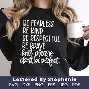 May include: A black sweatshirt with white text that reads "BE FEARLESS BE KIND BE RESPECTFUL BE BRAVE but please don't be perfect." The text is in a handwritten style. The sweatshirt is being worn by a person holding a white mug.