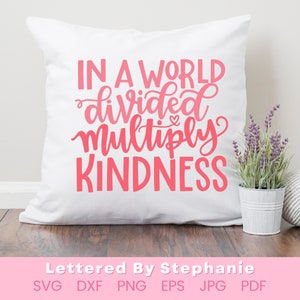 May include: A white pillow with pink lettering that reads "In a world divided multiply kindness".