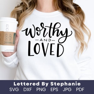 Op de afbeelding: Wit sweatshirt met de tekst "worthy -and- loved" in zwarte kalligrafie.