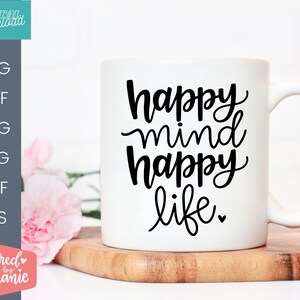 May include: White ceramic mug with black text that reads "happy mind happy life." The mug is sitting on a wooden surface.