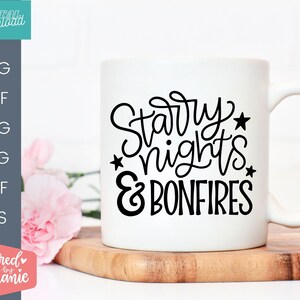 Op de afbeelding: Een witte keramische mok met zwarte tekst die "Starry Nights & Bonfires" zegt.