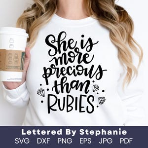 May include: White t-shirt with black text that reads "She is more precious than rubies" with diamond shapes around the text.