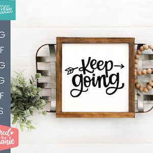 Op de afbeelding: Een houten bord met een witte achtergrond en zwarte tekst die "Keep going" zegt met een pijl die naar rechts wijst. Het bord staat op een houten oppervlak met een houten kist en een kralensnoer.
