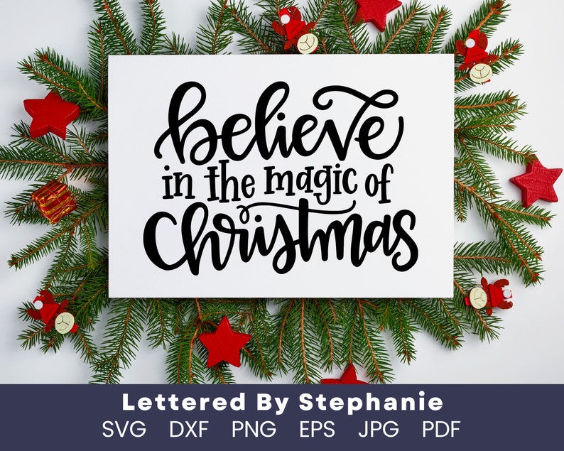 May include: A white sign with black text that reads "believe in the magic of Christmas" surrounded by green pine branches and red ornaments.