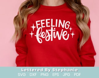 Puede incluir: Sudadera roja con texto blanco que dice "Feeling Festive" con dos estrellas blancas a cada lado del texto.