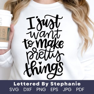 May include: White t-shirt with black text that reads "I just want to make pretty things". The text is in a handwritten font. The shirt is being held by a person. The text "Lettered By Stephanie" is below the design. The words "SVG DXF PNG EPS JPG PDF" are below the text.
