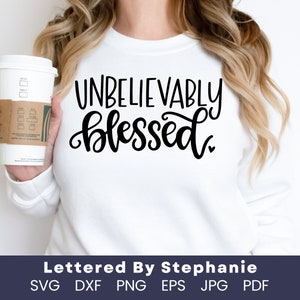 以下が含まれることがあります： 白いスウェットシャツに、黒い筆記体で「Unbelievably blessed」という文字が書かれています。文字はスウェットシャツの中央に配置されています。スウェットシャツは、コーヒーカップを持っている人が着用しています。