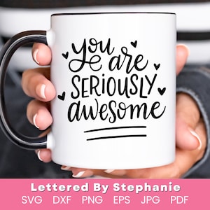 May include: White ceramic mug with a black handle. The mug has black lettering that reads "You are seriously awesome" with a heart symbol after each word. The mug is held by a hand.