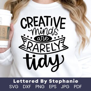 May include: A white sweatshirt with black text that reads "CREATIVE Minds are RARELY tidy". The text is in a handwritten font. The bottom of the sweatshirt has the text "Lettered By Stephanie" and "SVG DXF PNG EPS JPG PDF".