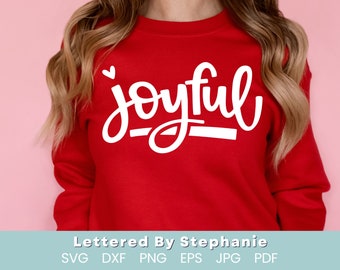 Puede incluir: Una sudadera roja con la palabra "joyful" escrita en letras blancas cursivas con un pequeño corazón sobre la palabra. La palabra está subrayada con una línea blanca.