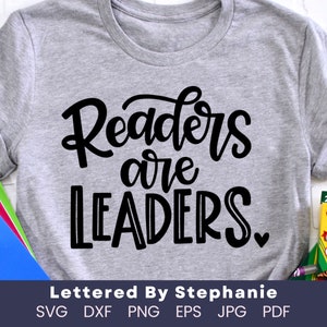 May include: A gray t-shirt with the text "Readers are LEADERS." in black lettering. The text is in a handwritten style. The t-shirt is on a white surface. The text "Lettered By Stephanie" is below the design. The text "SVG DXF PNG EPS JPG PDF" is below the text "Lettered By Stephanie".