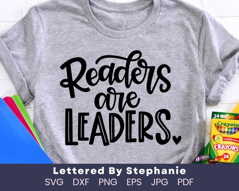 May include: A gray t-shirt with the text "Readers are LEADERS." in black lettering. The text is in a handwritten style. The t-shirt is on a white surface. The text "Lettered By Stephanie" is below the design. The text "SVG DXF PNG EPS JPG PDF" is below the text "Lettered By Stephanie".