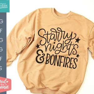 Op de afbeelding: Een beige sweatshirt met de tekst "Starry nights & bonfires" in zwarte letters. De tekst is in een handschrift met sterren eromheen.