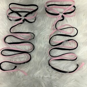 May include: Two black and pink ribbon choker necklaces with a silver heart charm. The ribbons are tied together at the back of the neck.