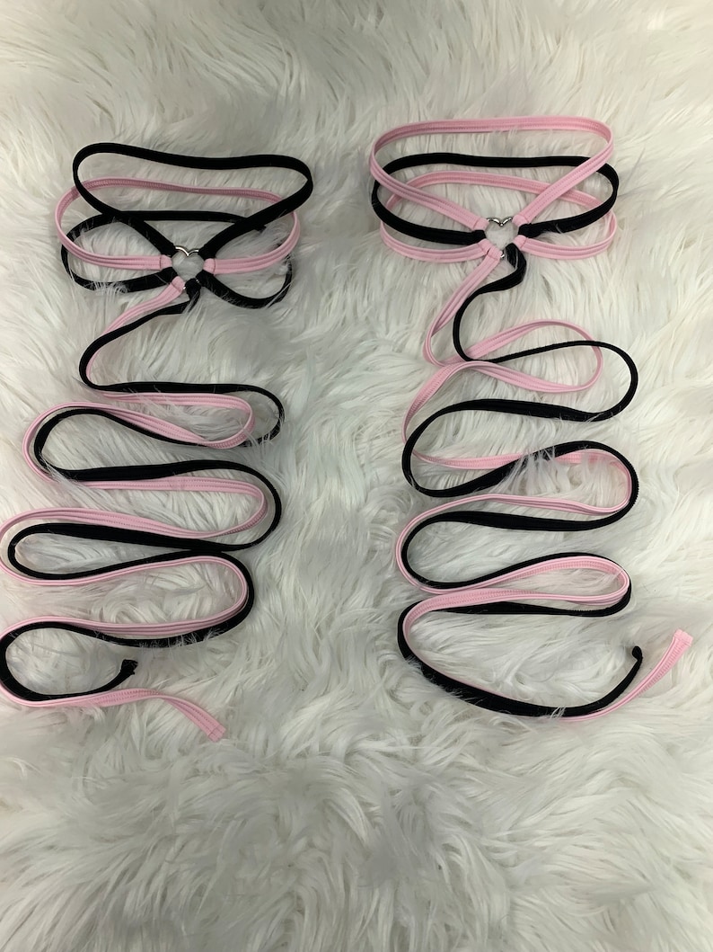 May include: Two black and pink ribbon choker necklaces with a silver heart charm. The ribbons are tied together at the back of the neck.