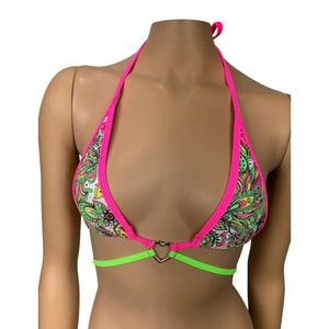 May include: A halter-style bikini top with a vibrant paisley pattern in green, yellow, and pink on a white background. The edges are trimmed in bright pink, with a neon green underbust band and a silver heart-shaped connector.